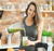 Woman pouring green smoothie from blender into a jar in a bright kitchen setting.