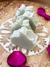 Handcrafted phytoplankton infused soap bars on a wooden surface, surrounded by pink rose petals and sea salt.